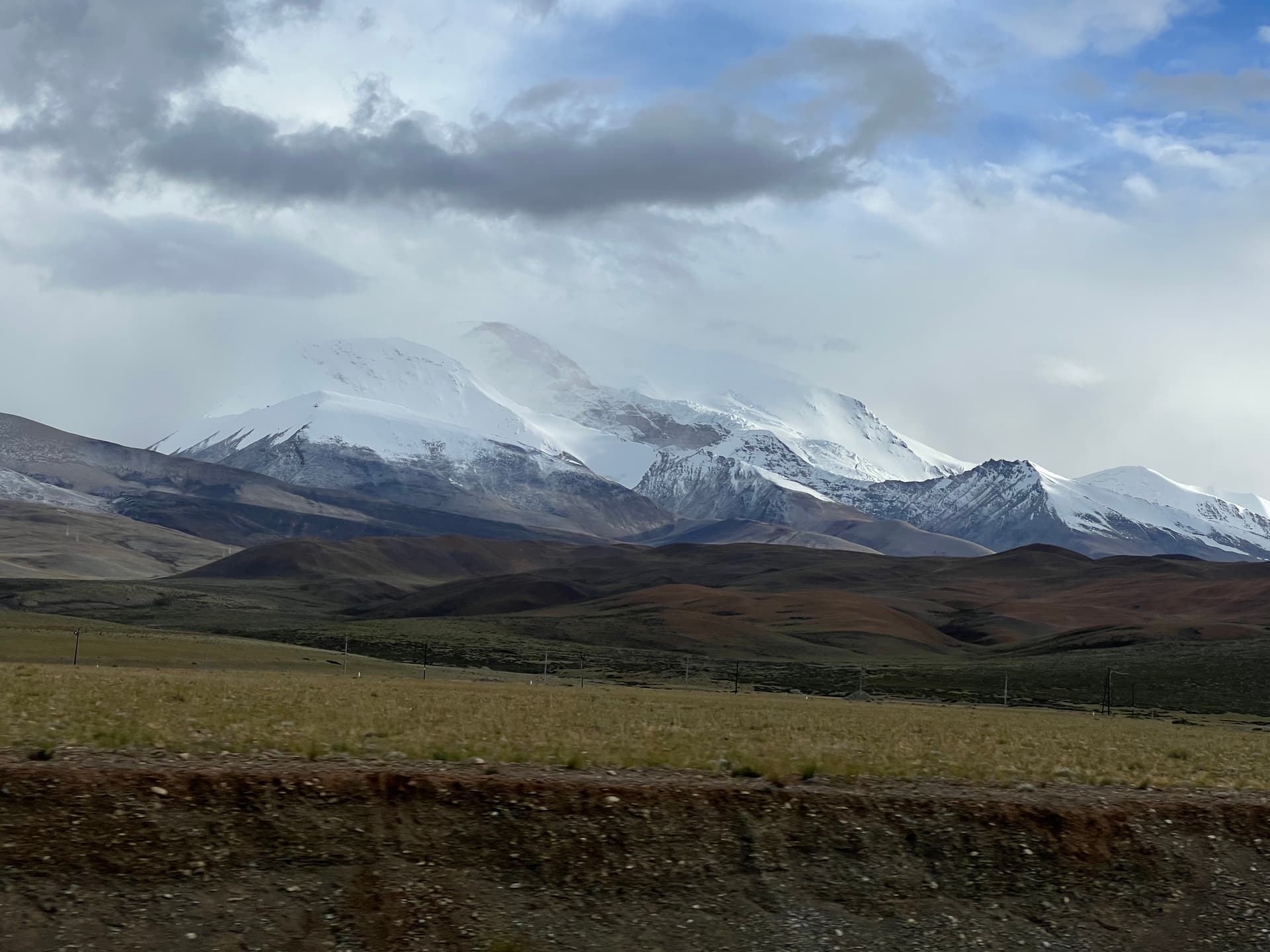 Snow-capped Himalayan range viewed across the Tibetan plateau with clouds rolling over the peaks