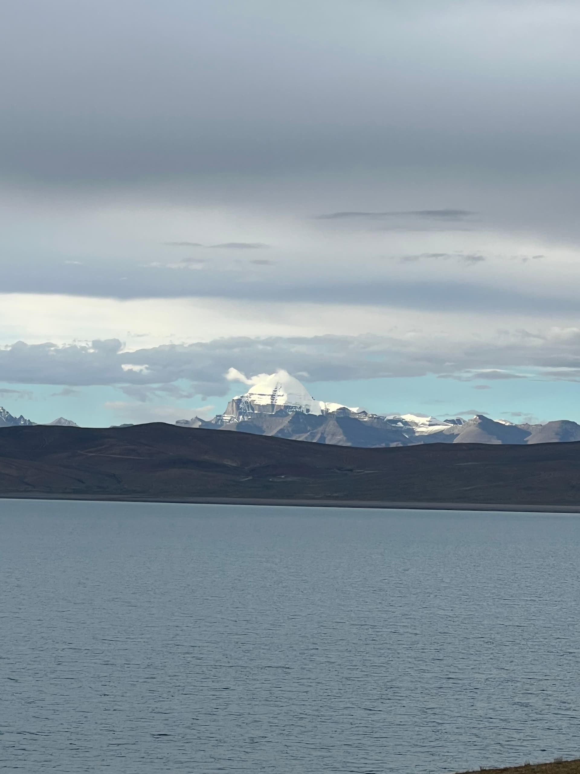 Mount Kailash seen across Lake Mansarovar from the shore, peak rising above distant hills
