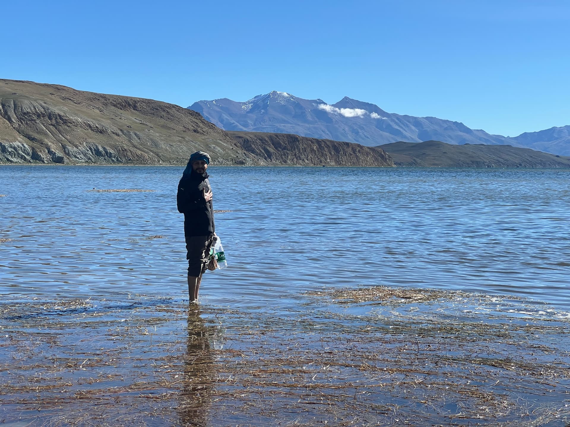 Pilgrim standing in the shallow waters of Lake Mansarovar with hand over heart, snow peaks behind