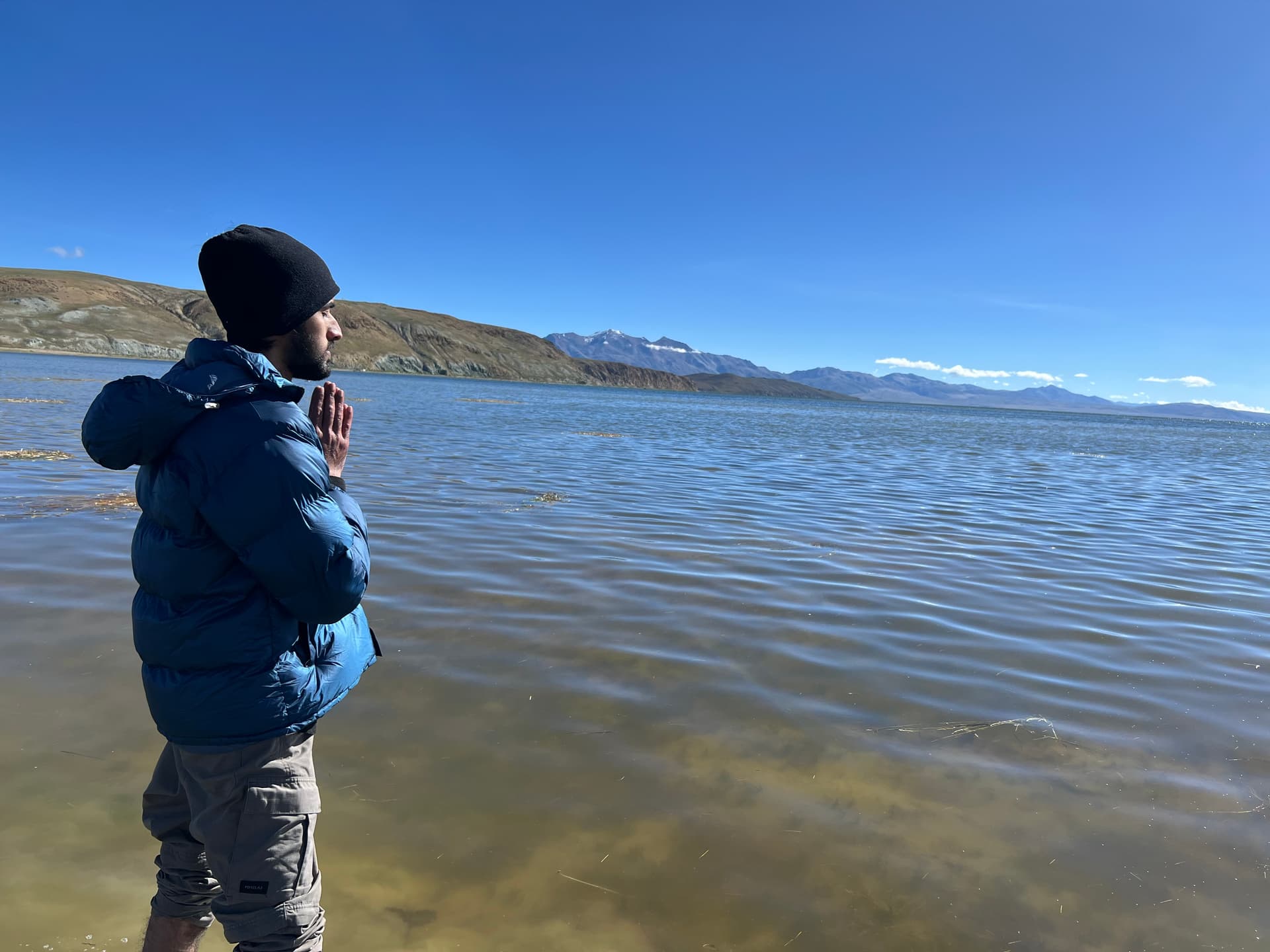 Suryansh offering prayers at Lake Mansarovar with snow-capped peaks in the distance