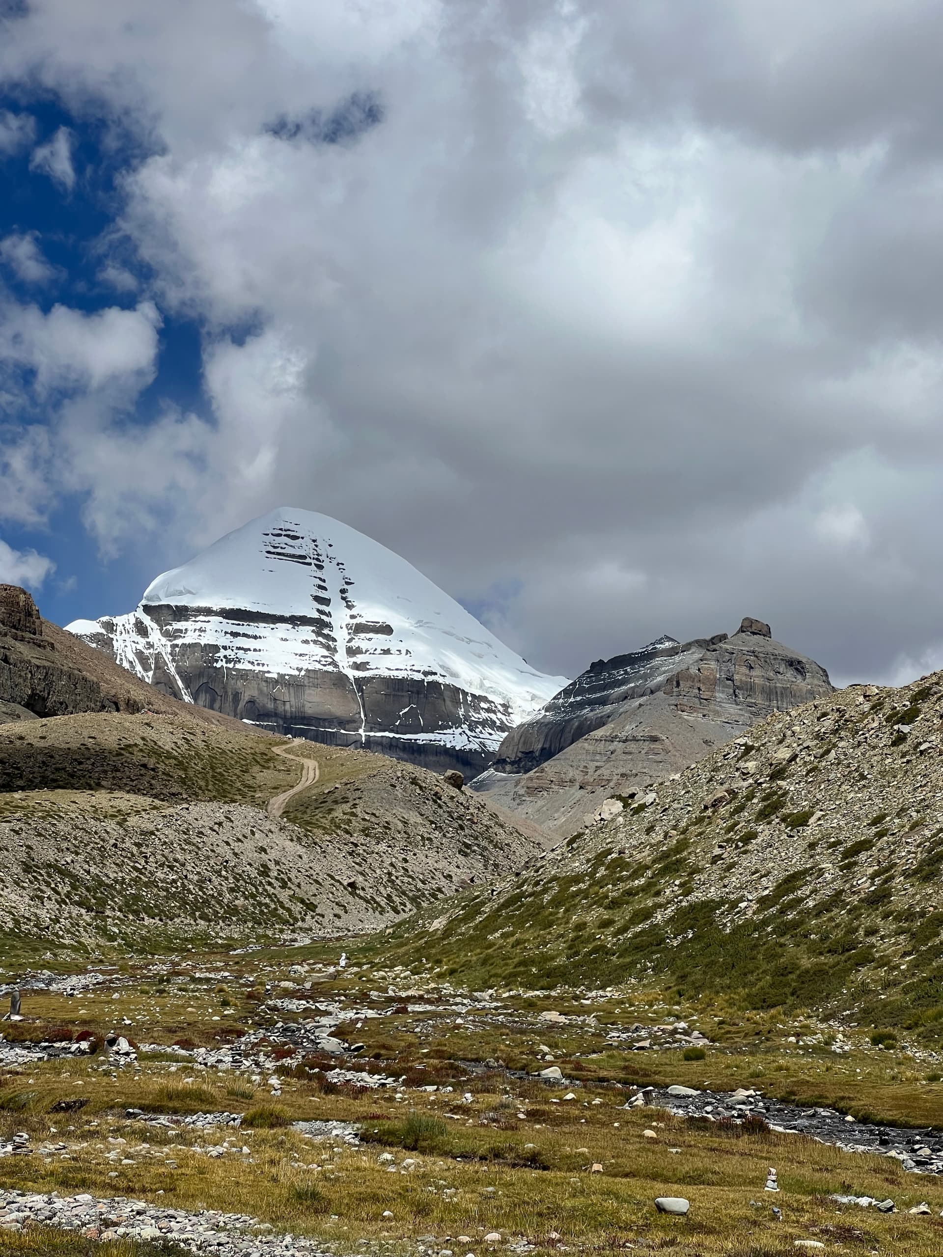 Mount Kailash towering over the kora valley with a stream and pilgrimage trail winding below