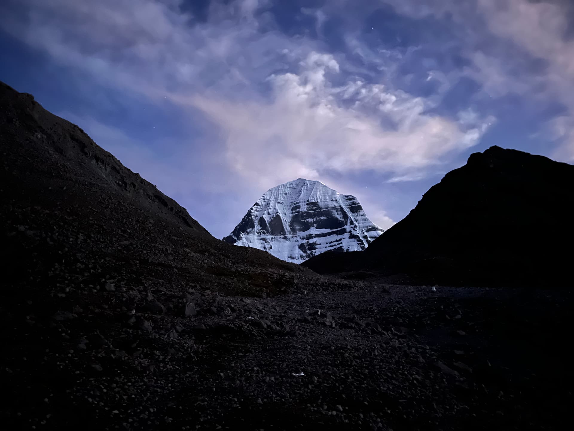 Mount Kailash at twilight, snow-lit peak framed by dark valley slopes under a starry sky