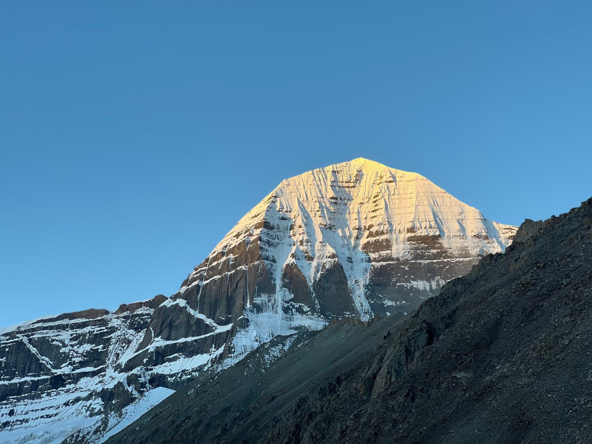 Golden light on Mount Kailash peak at sunrise against a clear blue Himalayan sky