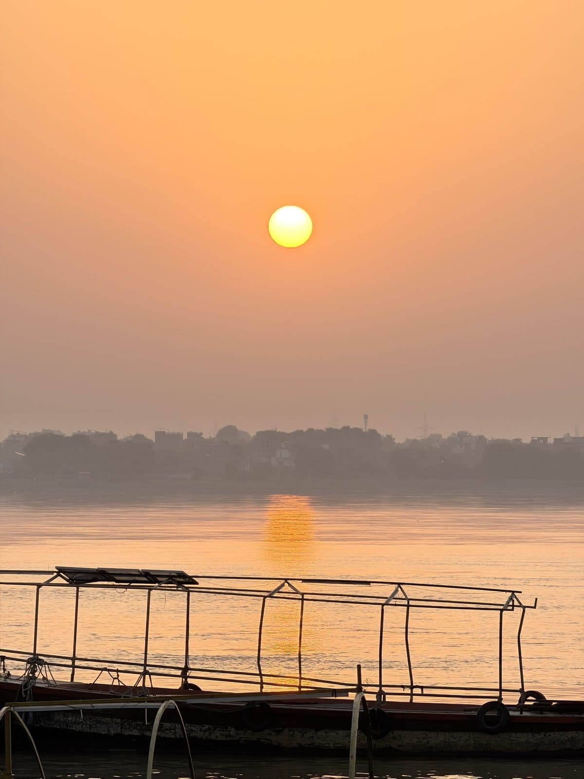 The sun rising through the haze over the Ganga, its reflection a gold path on the water, a moored boat in the foreground