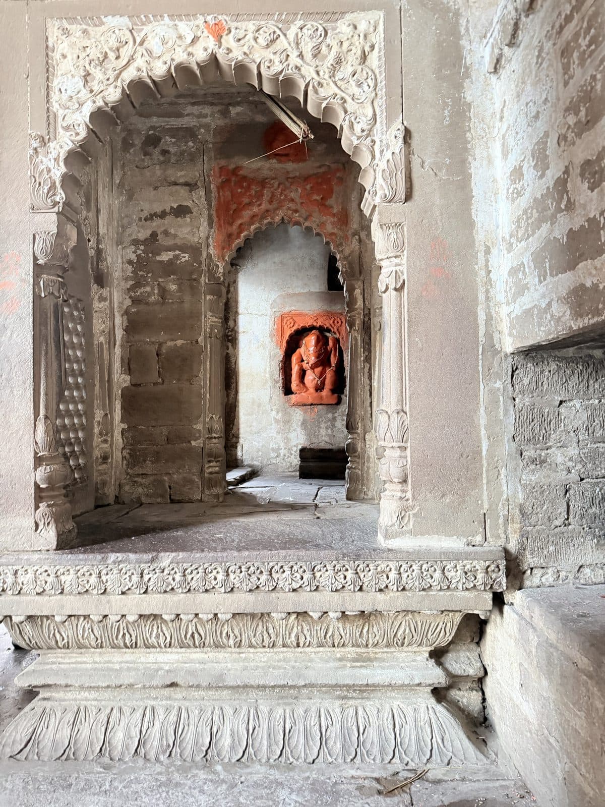 A small sindoor-covered Ganesha deep inside a carved sandstone shrine, seen through two scalloped arches