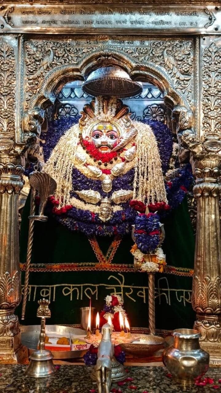 Baba Kaal Bhairav's silver face in a carved silver shrine, draped in white and violet garlands, with lamps lit before him