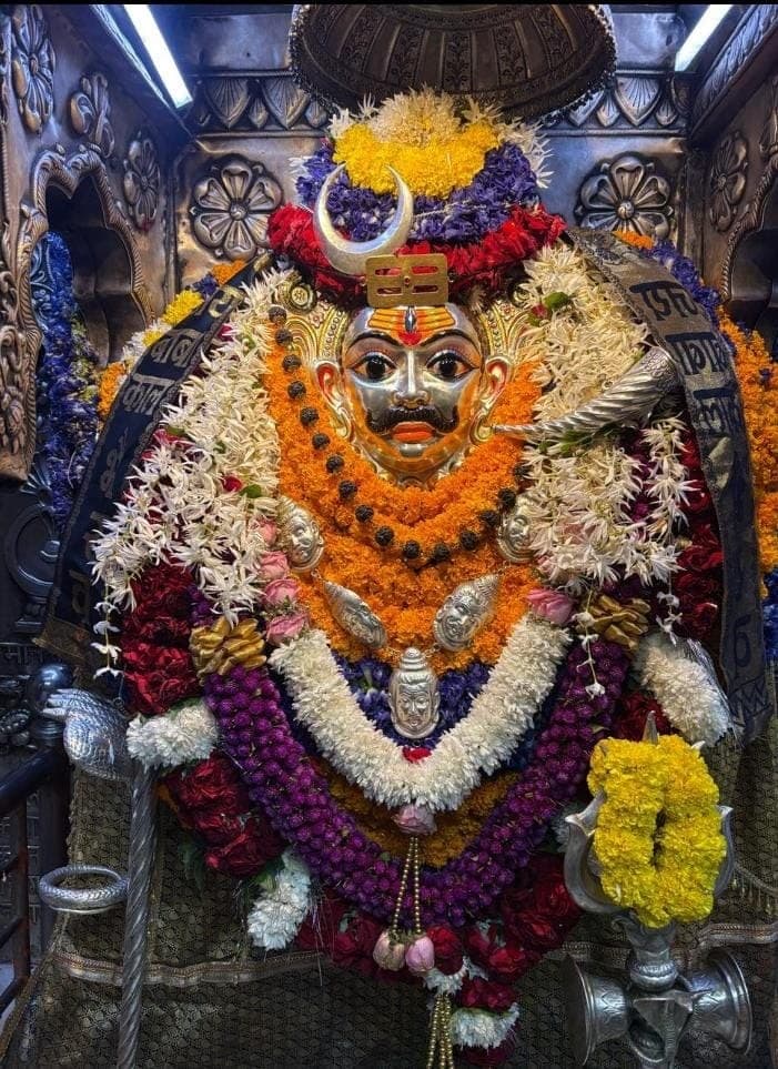 Kaal Bhairav's silver face in the sanctum, crowned with a crescent moon and wrapped in garlands of marigold, rose, jasmine and purple flowers