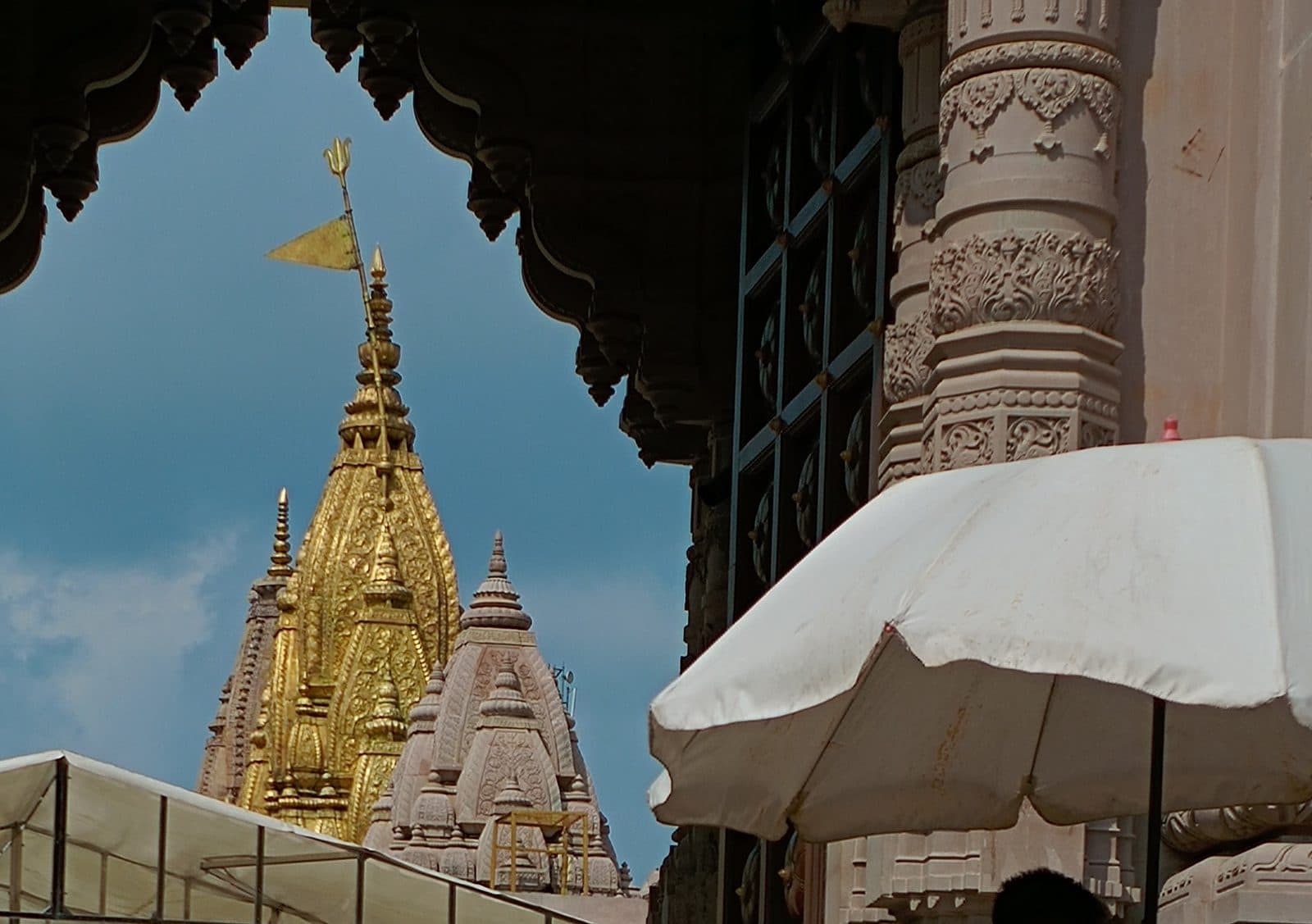 The gold-plated shikhara of the Kashi Vishwanath temple framed by a carved stone archway against a blue sky