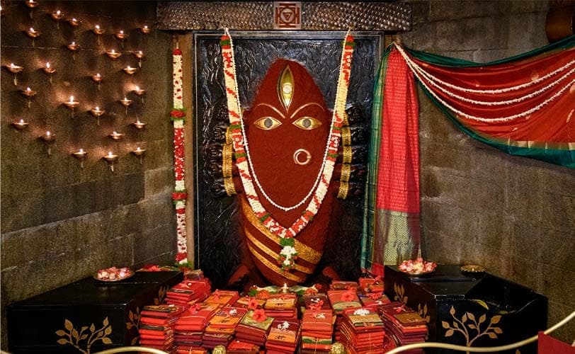 Linga Bhairavi in red, with saris offered at her feet and lamps lit around her