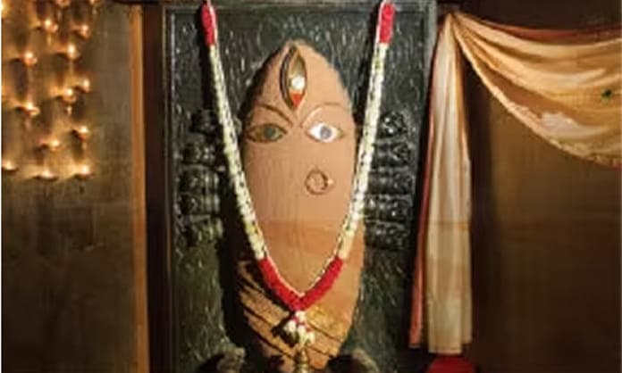 Linga Bhairavi adorned in cream and white, lit by oil lamps