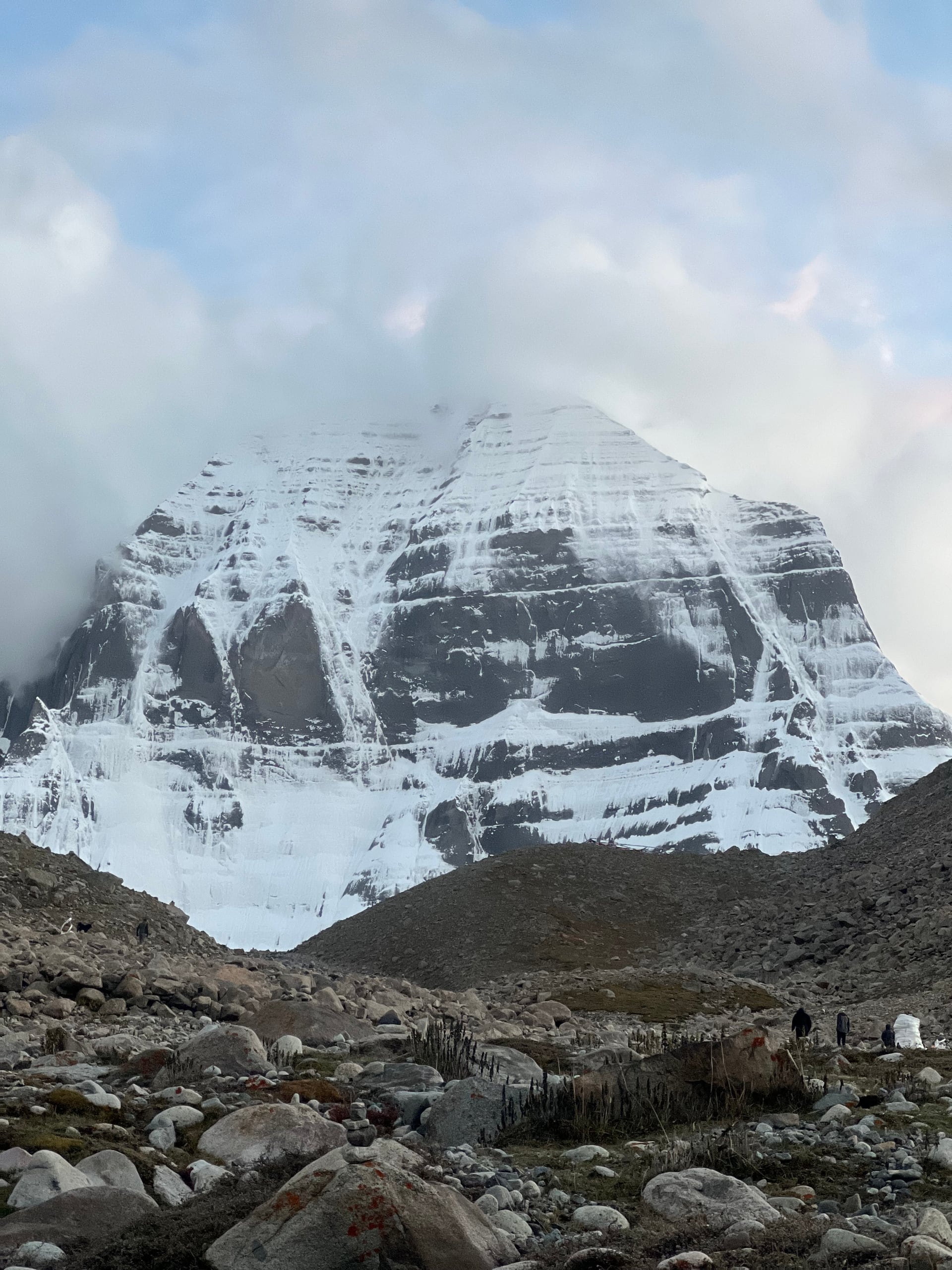 Mount Kailash north face seen from the rocky parikrama trail with pilgrims and a stone cairn in the foreground