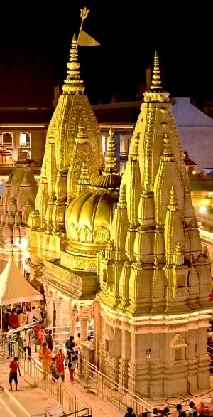 The gold-spired Shri Kashi Vishwanath Temple lit up at night, with pilgrims on the steps below